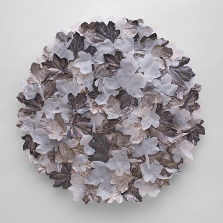 round wall artwork covered in stacked field maple leaves each riveted in place and made from milky white plastic oxidised silver and roughed aluminium cans